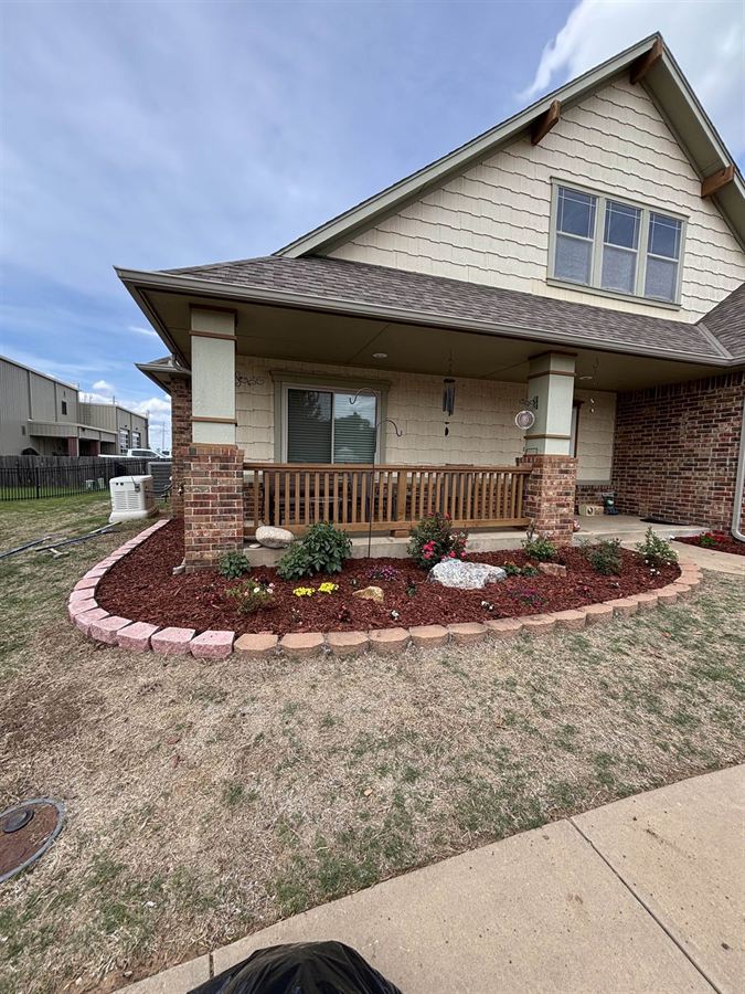 Curved flower bed with stone block border, fresh orange mulch, and new flowers along a front porch