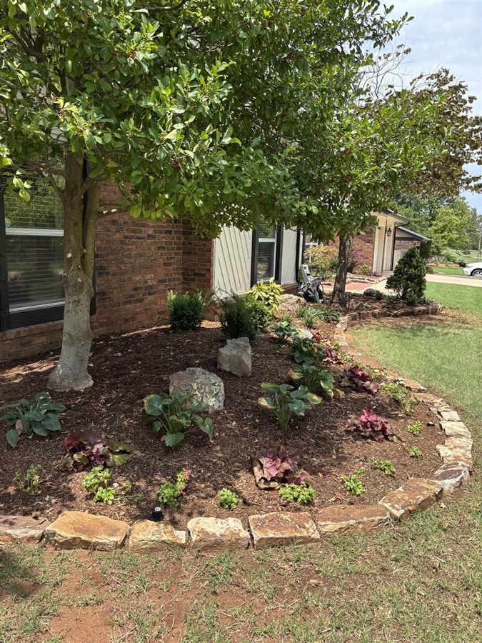 Large curved garden bed edged in natural stone with fresh mulch and new plantings