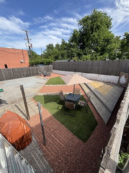 The same backyard finished with clean turf panels, red decorative gravel, river rock borders, and patio furniture