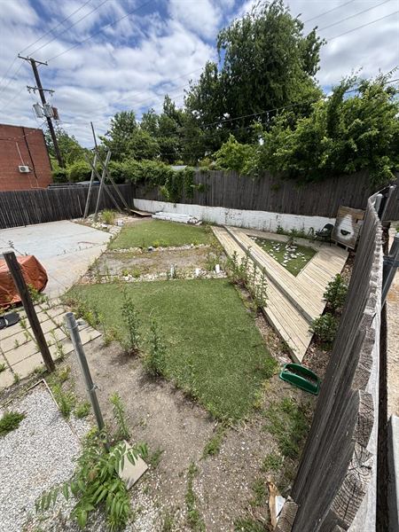 Backyard before the work, with weeds coming through the patio, bare dirt, and an overgrown fence line