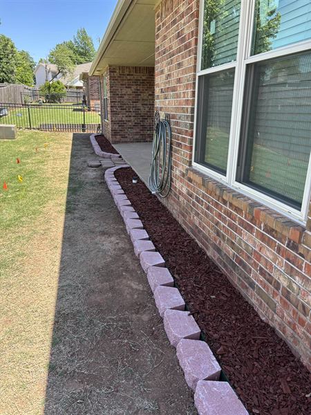 Stone bordered mulch bed along the back of a brick home