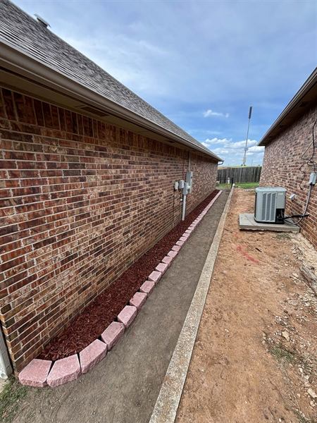 Mulch bed with stone block border running along the side of a brick house