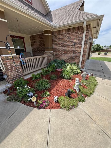 Front garden bed with orange mulch, hostas, flowers, and garden statues
