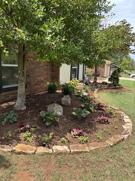 Large curved garden bed edged in natural stone with mulch and new plantings