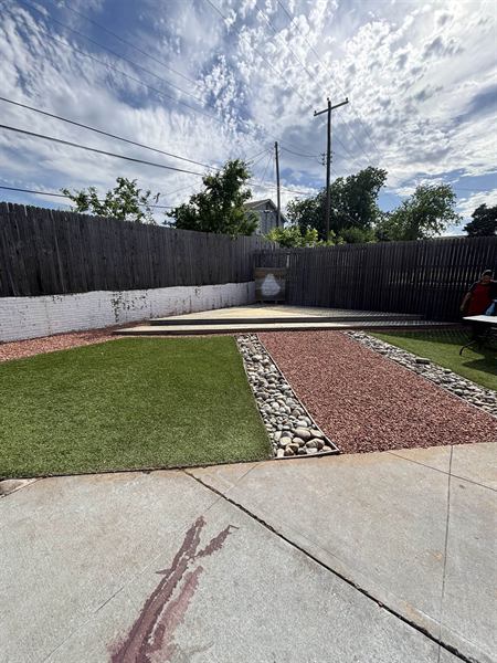 Backyard with artificial turf panels, red gravel, and river rock borders