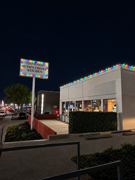 Restaurant at night with red, green, blue, and orange lights along the roofline and around the street sign